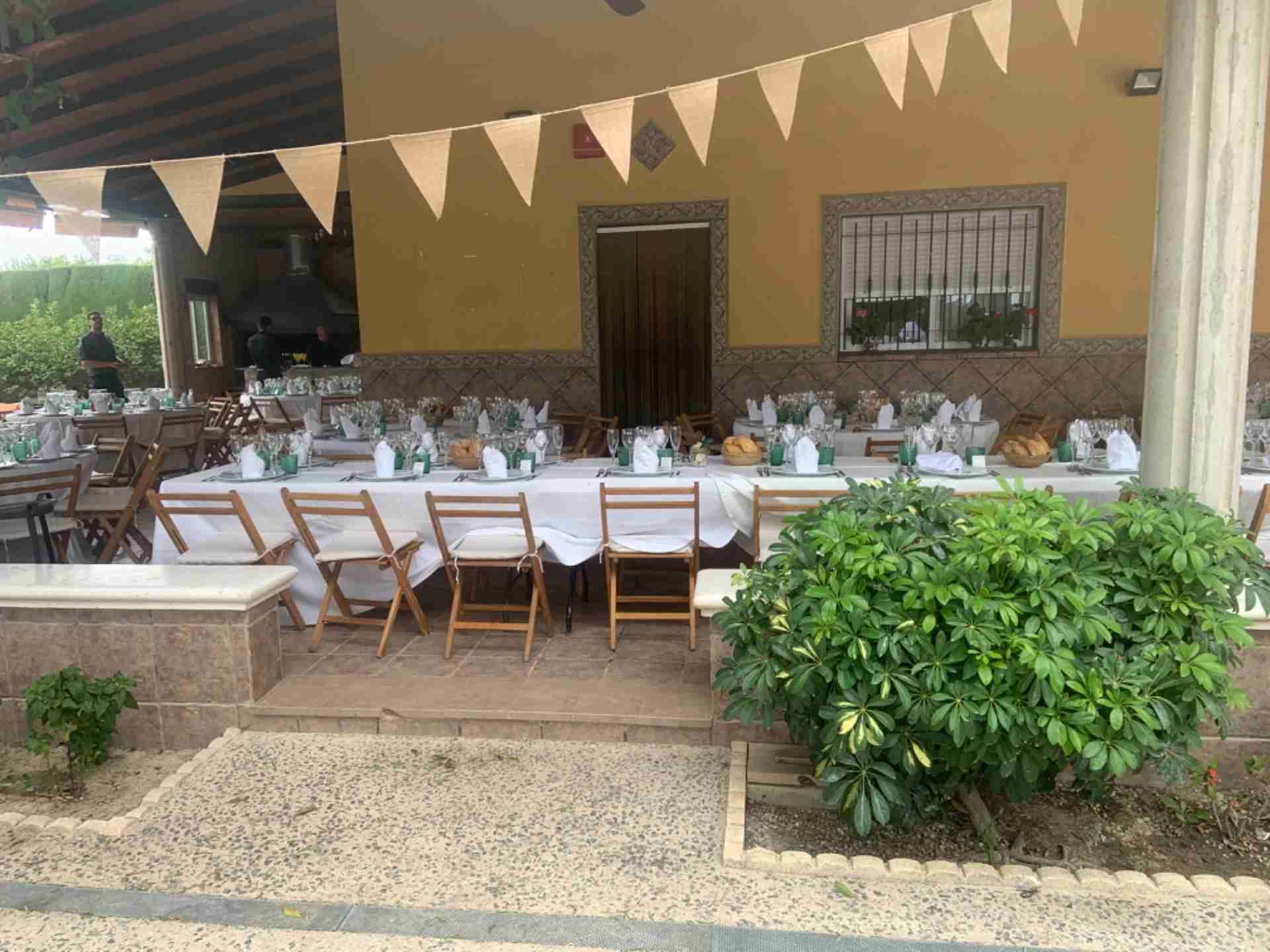 Evento al aire libre con largas mesas dispuestas para cenar bajo un toldo color canela, decoradas con banderines.