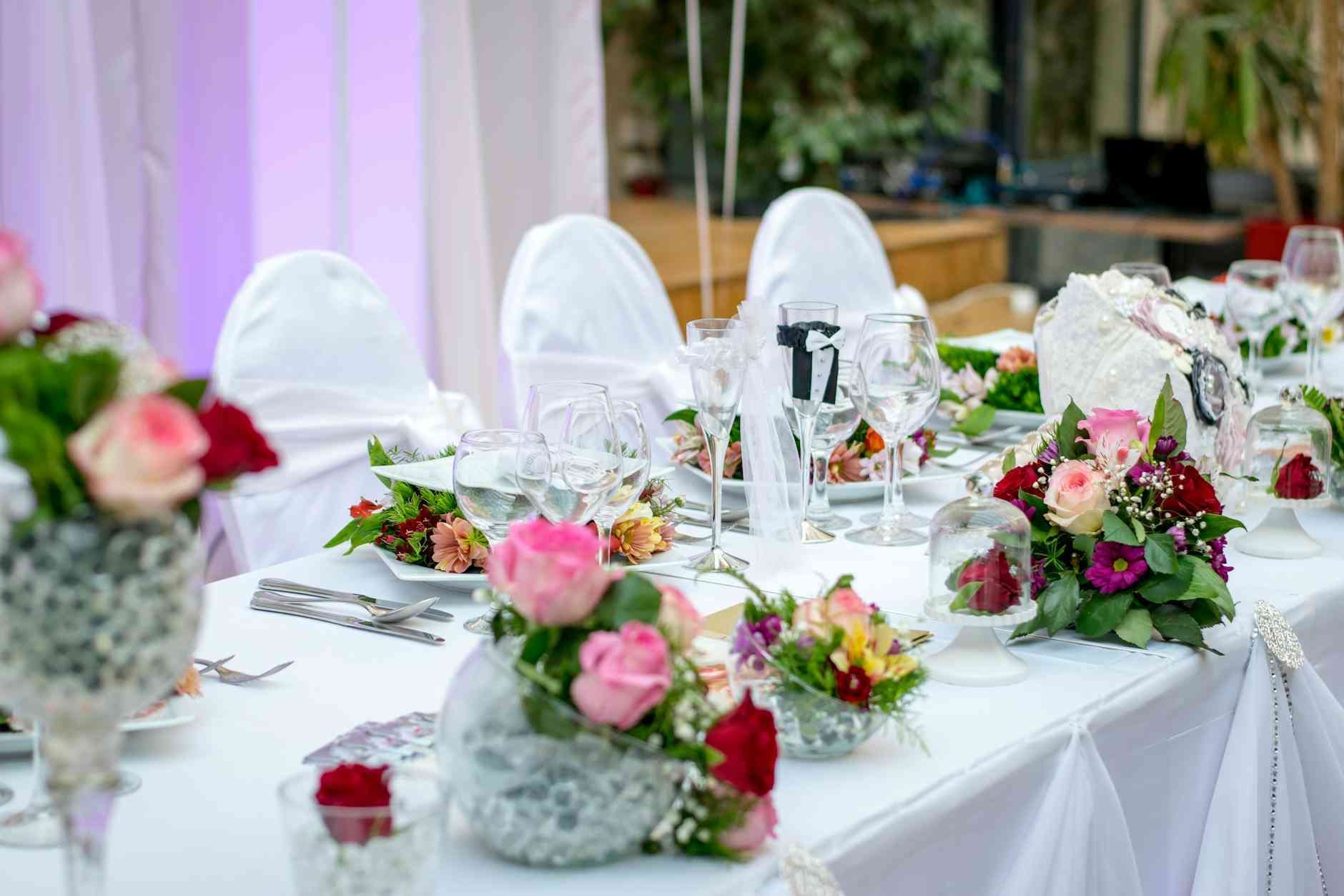 Mesa de recepción de boda preparada con flores, cubiertos y sillas cubiertas.