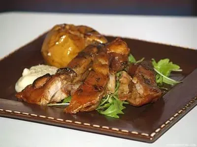 Cerdo asado y manzana al horno en un plato marrón con verduras y salsa.