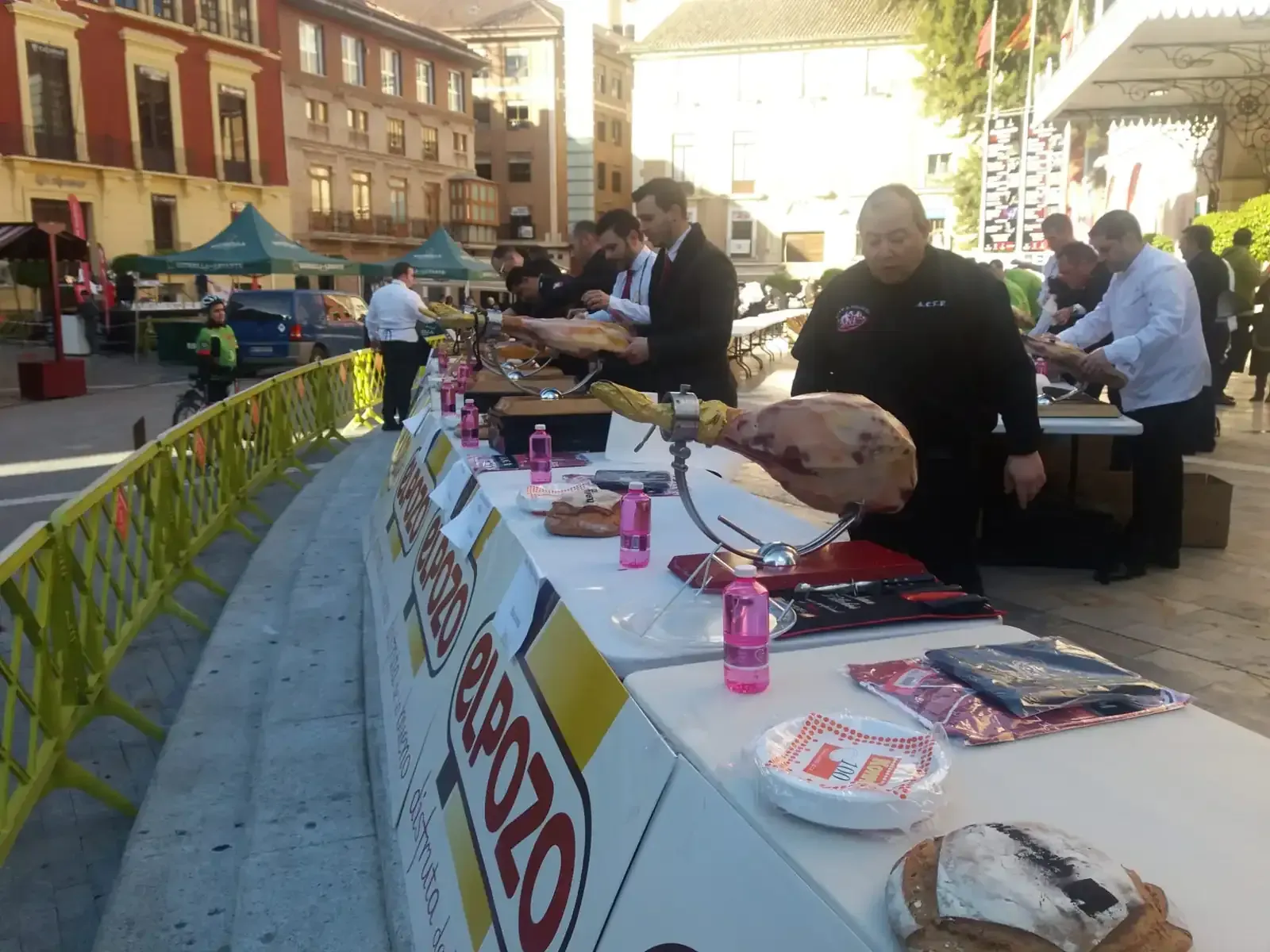 Gente cortando e inspeccionando jamón en un evento gastronómico al aire libre con mesas.