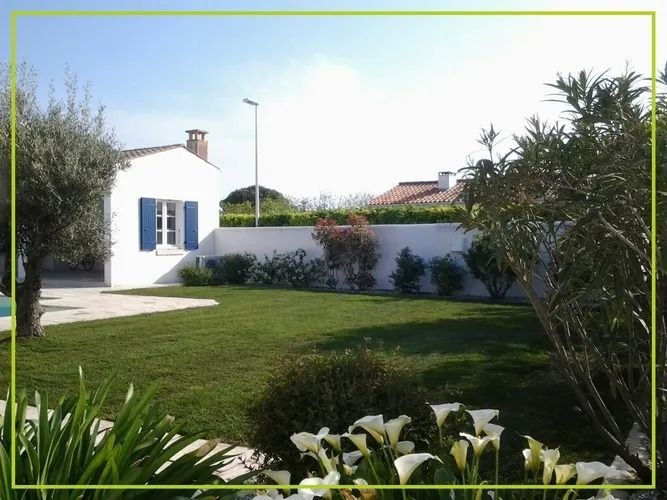Une maison blanche aux volets bleus, une pelouse verte et des fleurs sous un ciel ensoleillé