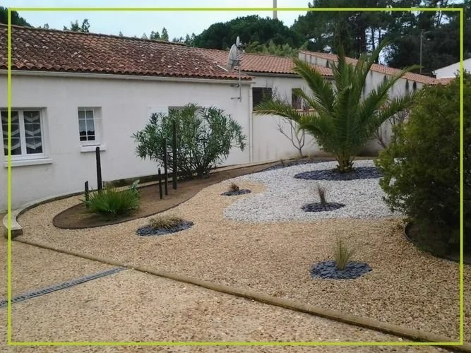 Un jardin recouvert de gravier avec un palmier et une maison blanche en arrière-plan