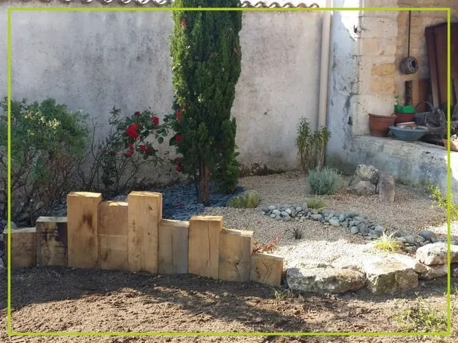 Un petit jardin avec une bordure en bois, des plantes et un cipres