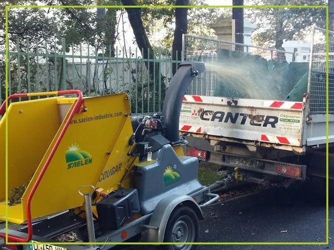 Une déchiqueteuse à bois montée sur une remorque et qui projette des copeaux de bois dans la benne d'un camion