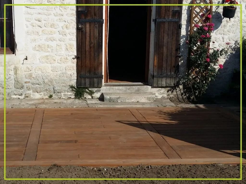 Terrasse en bois devant une maison en pierre avec volets et porte en bois