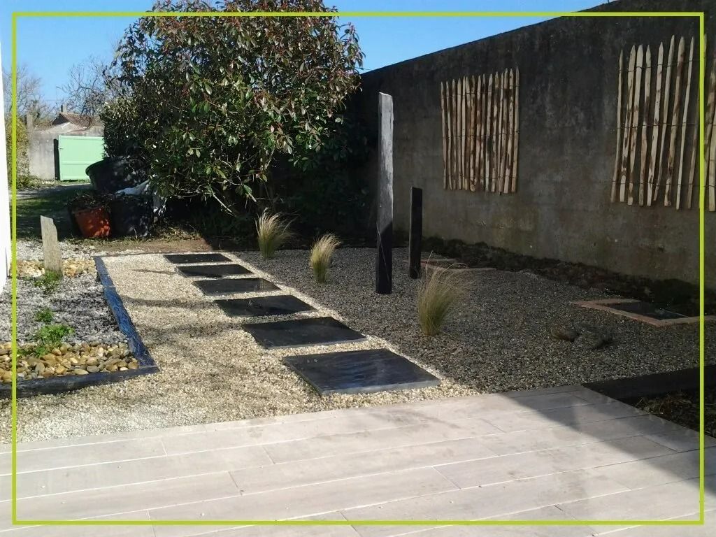 Allée de pierres dans un jardin de gravier, dalles carrées noires, fontaine, mur décoratif en bambou