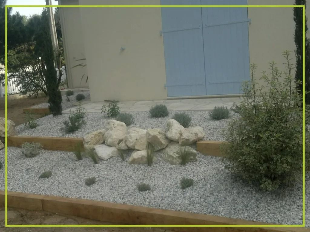 Massif de jardin aménagé avec rochers, gravier et plantes devant une maison aux volets bleus