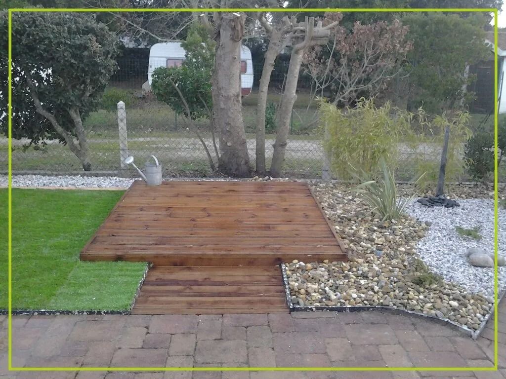 Terrasse en bois et gazon artificiel dans un jardin avec des galets et des arbres