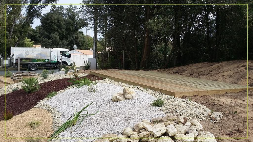 Aménagement paysager avec un lit de gravier, un mur de soutènement et un camion en arrière-plan