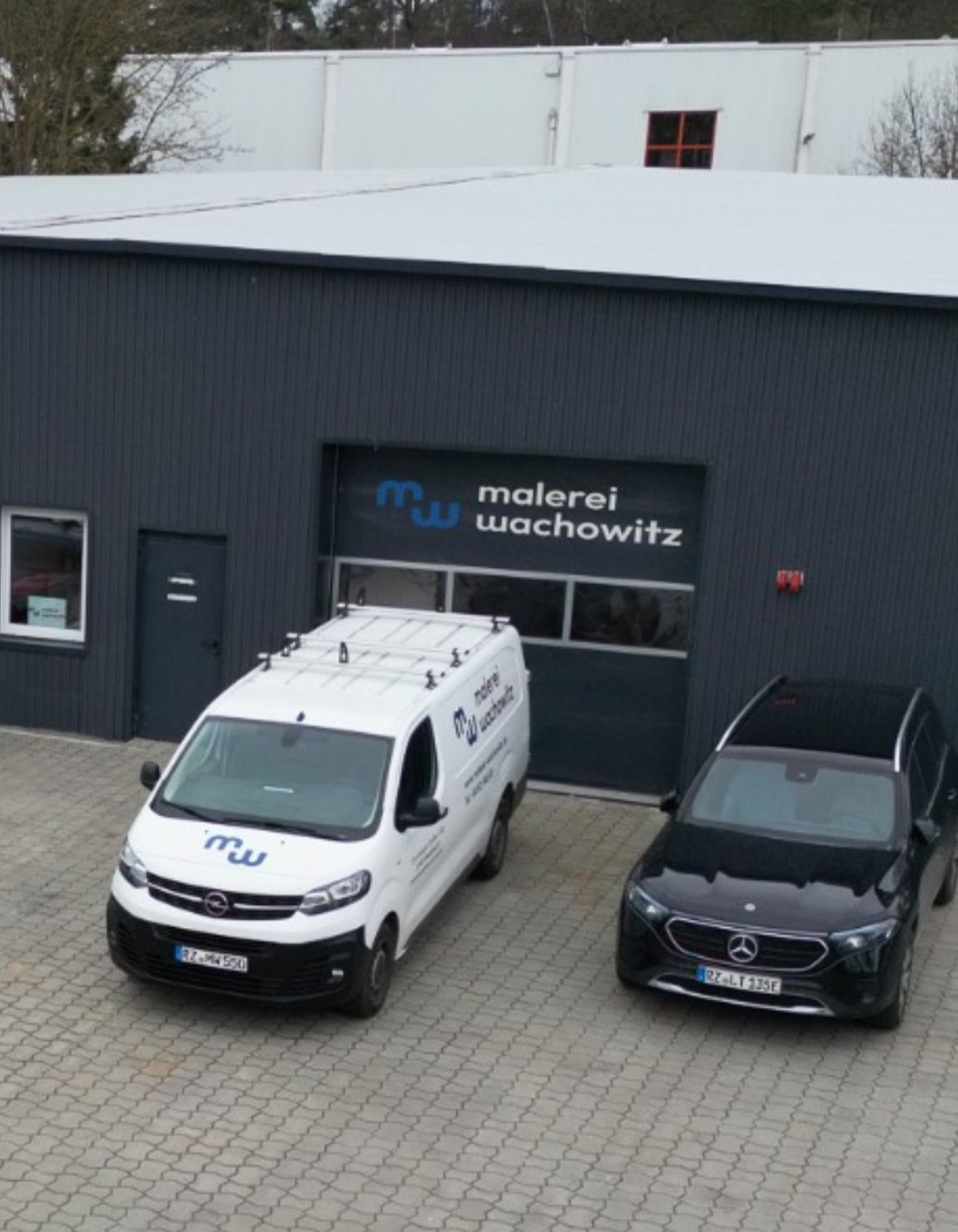 Ein weißer Lieferwagen und ein schwarzes Auto parken vor einem Gebäude.