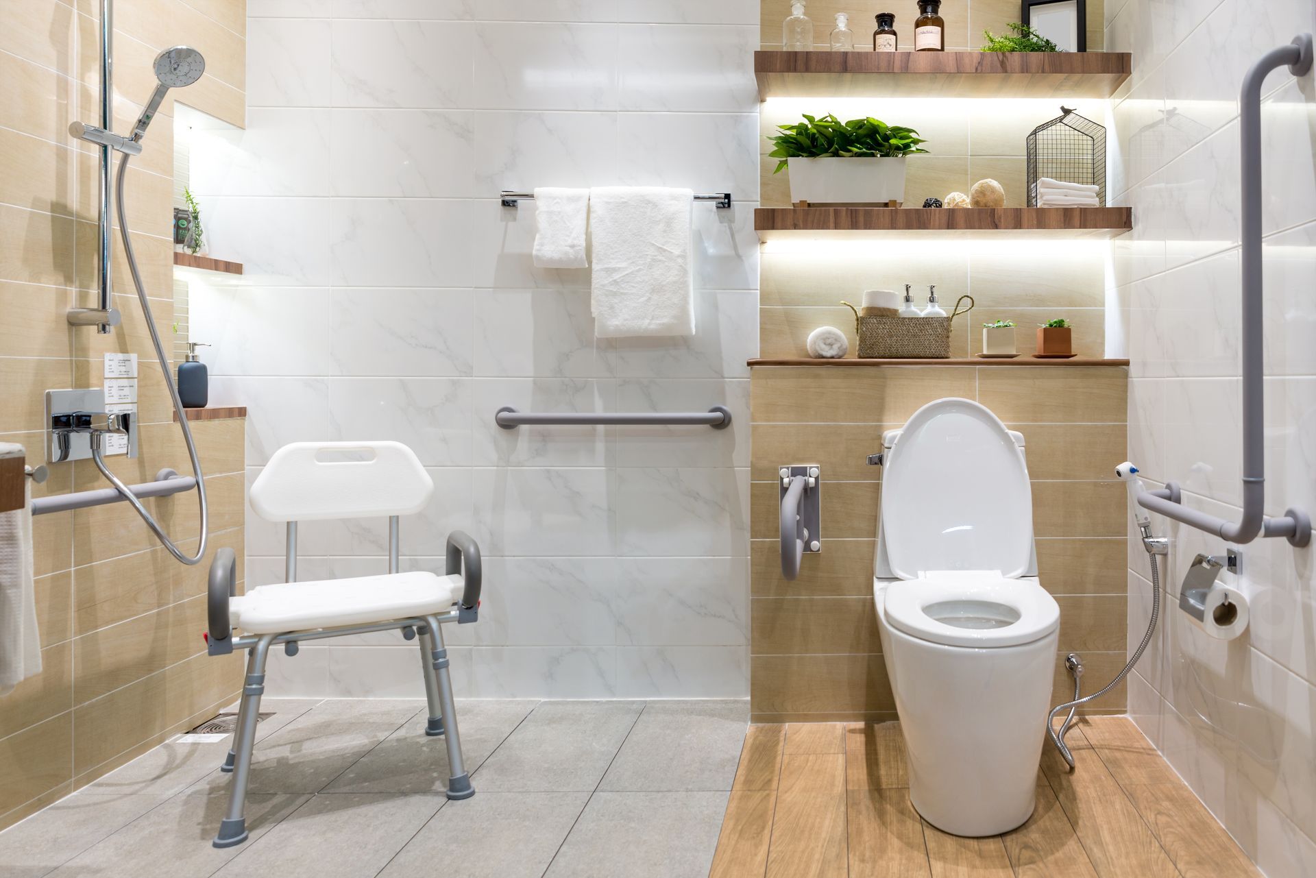 Une salle de bains moderne et accessible, avec un siège de douche blanc, des toilettes, des barres d'appui et des étagères en bois.