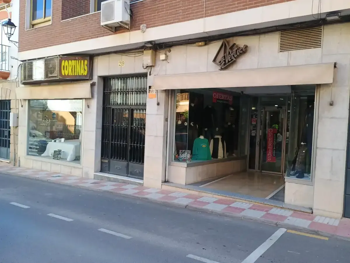 Persona cosiendo tela con una máquina de coser; tela sujetada con alfileres y herramientas visibles sobre una mesa blanca.