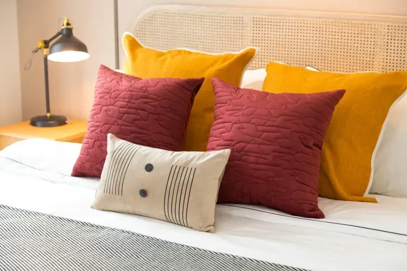 Cama con almohadas amarillas y rojas y una pequeña almohada decorativa.