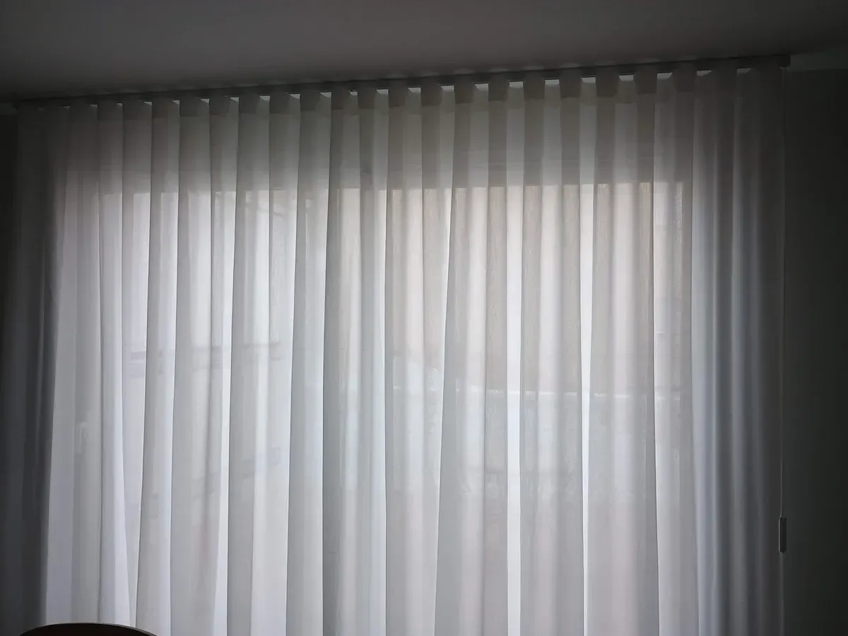 Persona cosiendo tela con una máquina de coser; tela sujetada con alfileres y herramientas visibles sobre una mesa blanca.