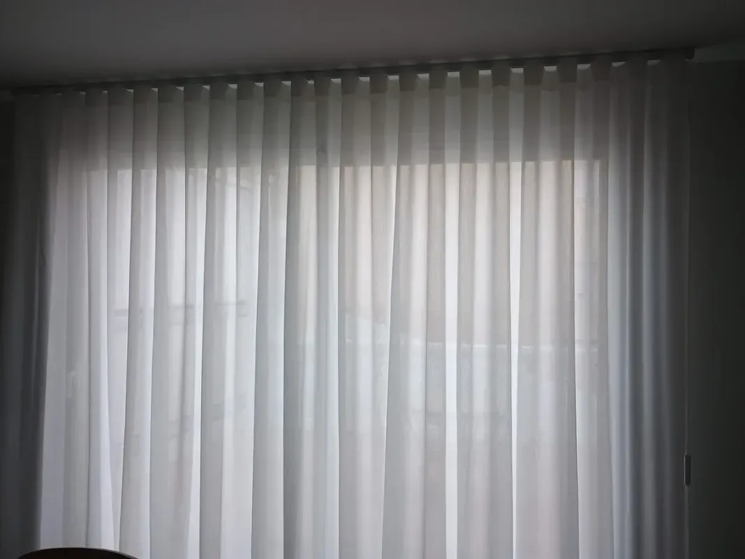 Persona cosiendo tela con una máquina de coser; tela sujetada con alfileres y herramientas visibles sobre una mesa blanca.