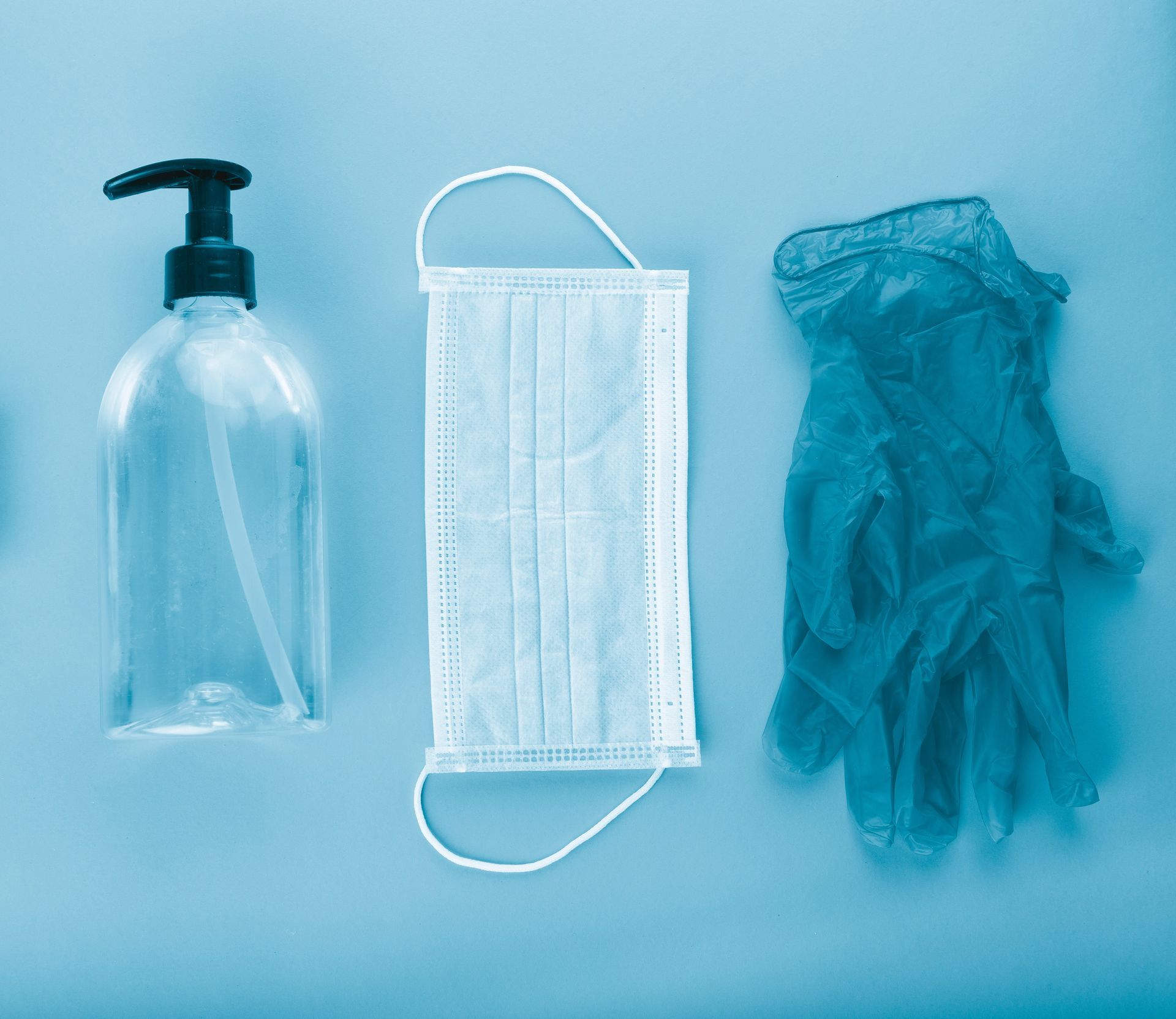Una mascarilla, guantes y una botella de desinfectante de manos sobre una superficie azul.