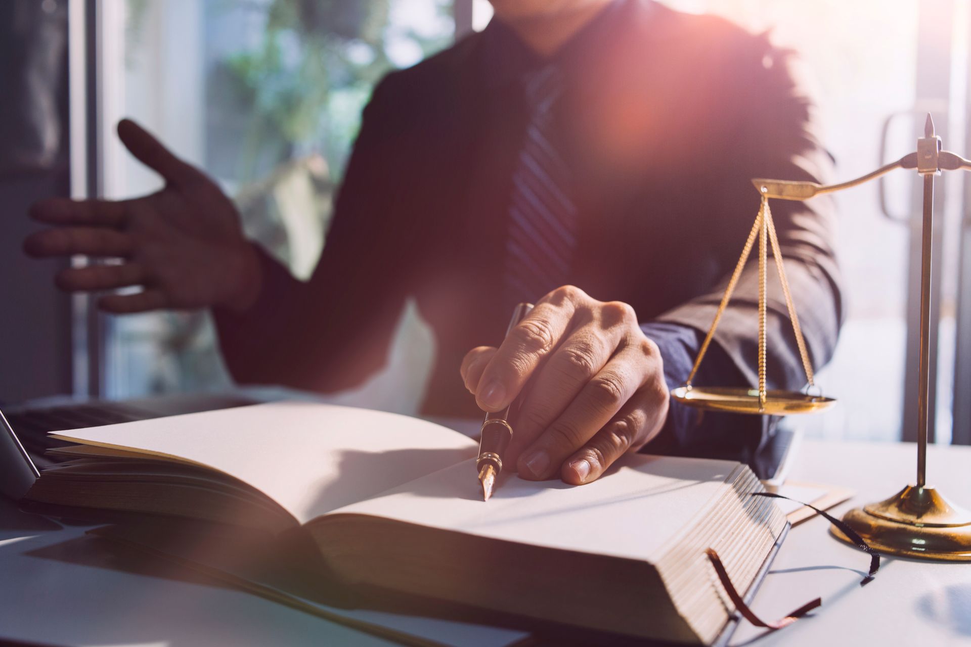 Persona con traje escribiendo en un libro abierto al lado de una balanza.