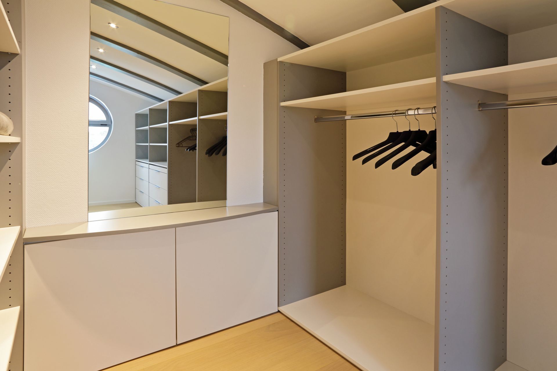 Dressing avec étagères intégrées, tringles et miroir. Intérieur clair avec cintres noirs.