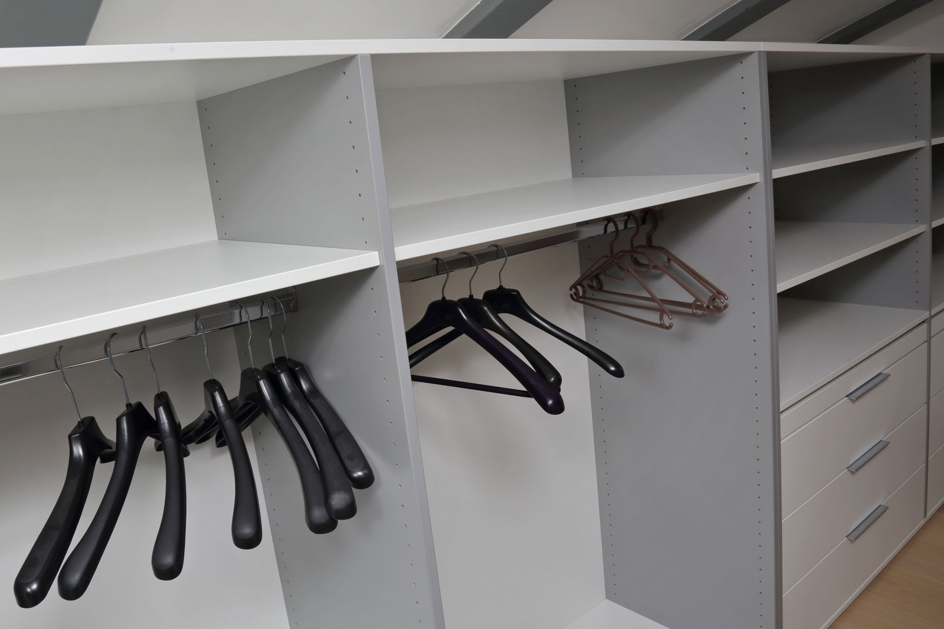 Placard blanc intégré avec étagères et tringles ; cintres noirs et argentés ; supports gris ; tiroirs.