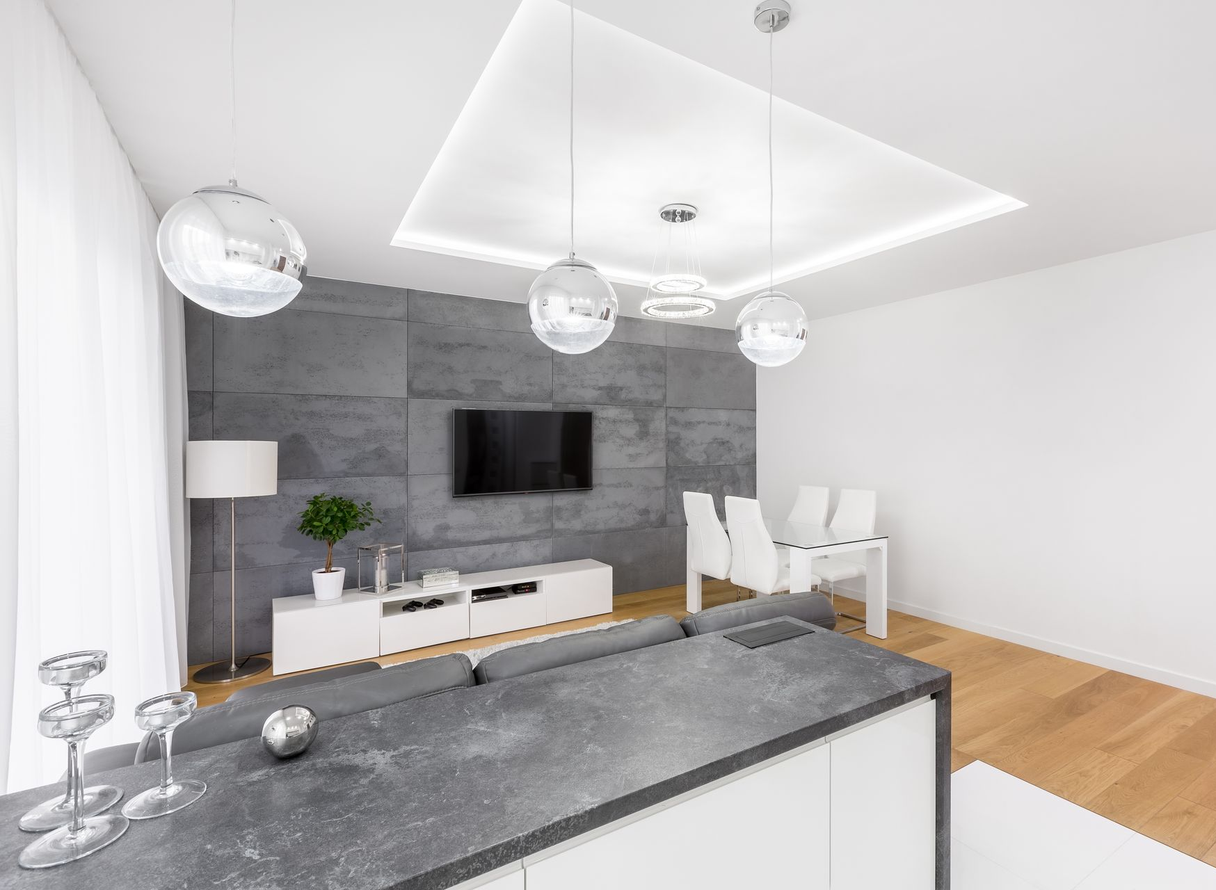 Salon moderne avec un mur d'accent gris, une télévision et des suspensions lumineuses. Mobilier blanc et parquet.