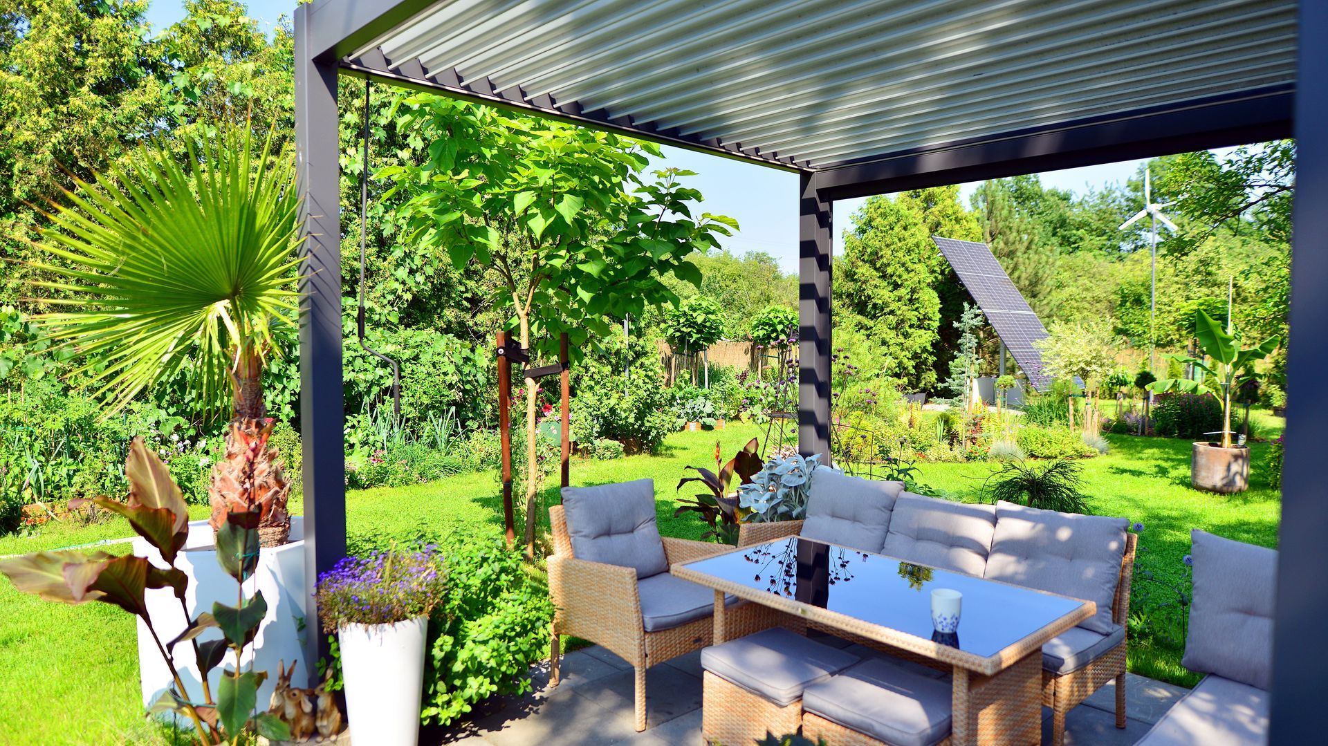 Terrasse avec mobilier en osier sous une pergola ; jardin verdoyant et luxuriant en arrière-plan.