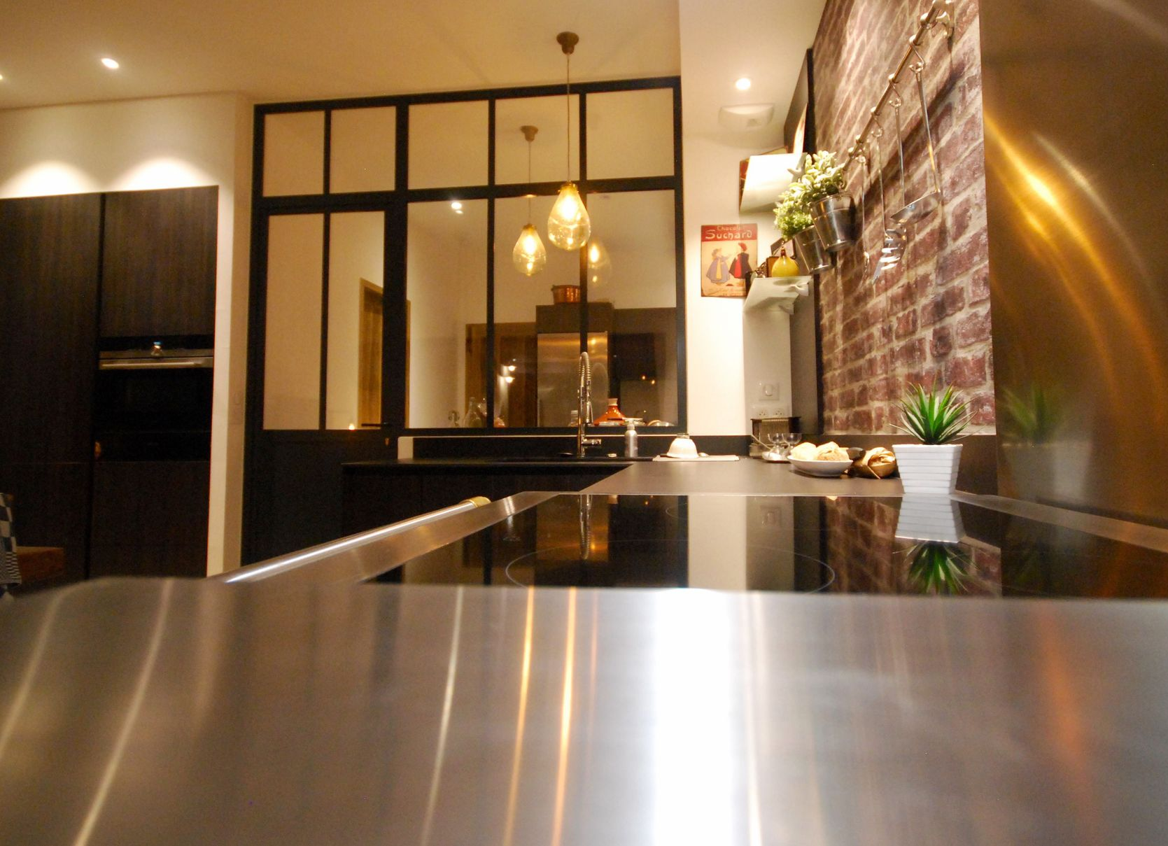 Cuisine moderne avec comptoir en acier inoxydable, mur en briques apparentes et armoires foncées.