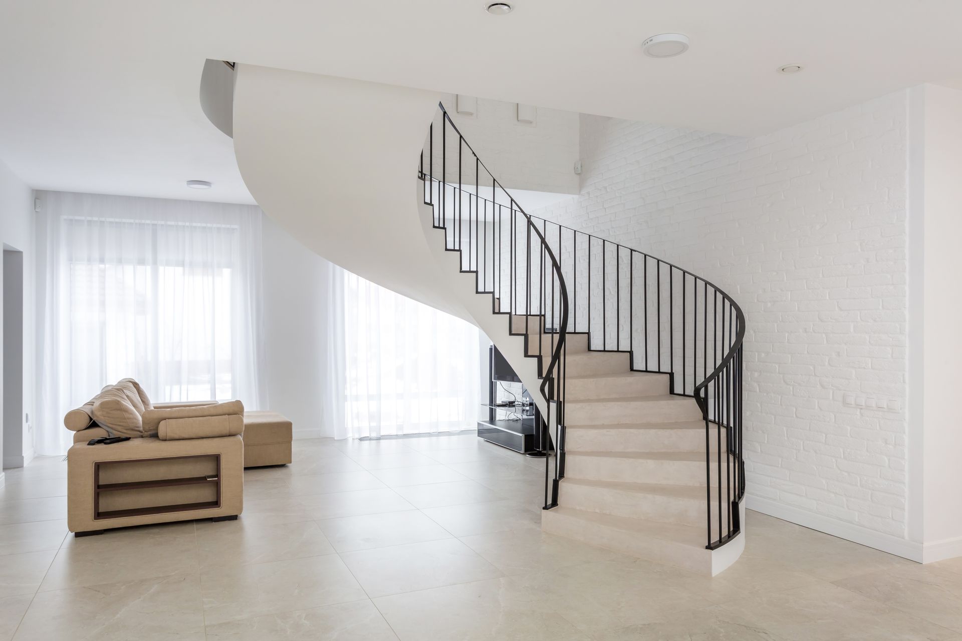 Un escalier blanc incurvé avec une rampe noire mène à l'étage dans une pièce moderne et lumineuse.