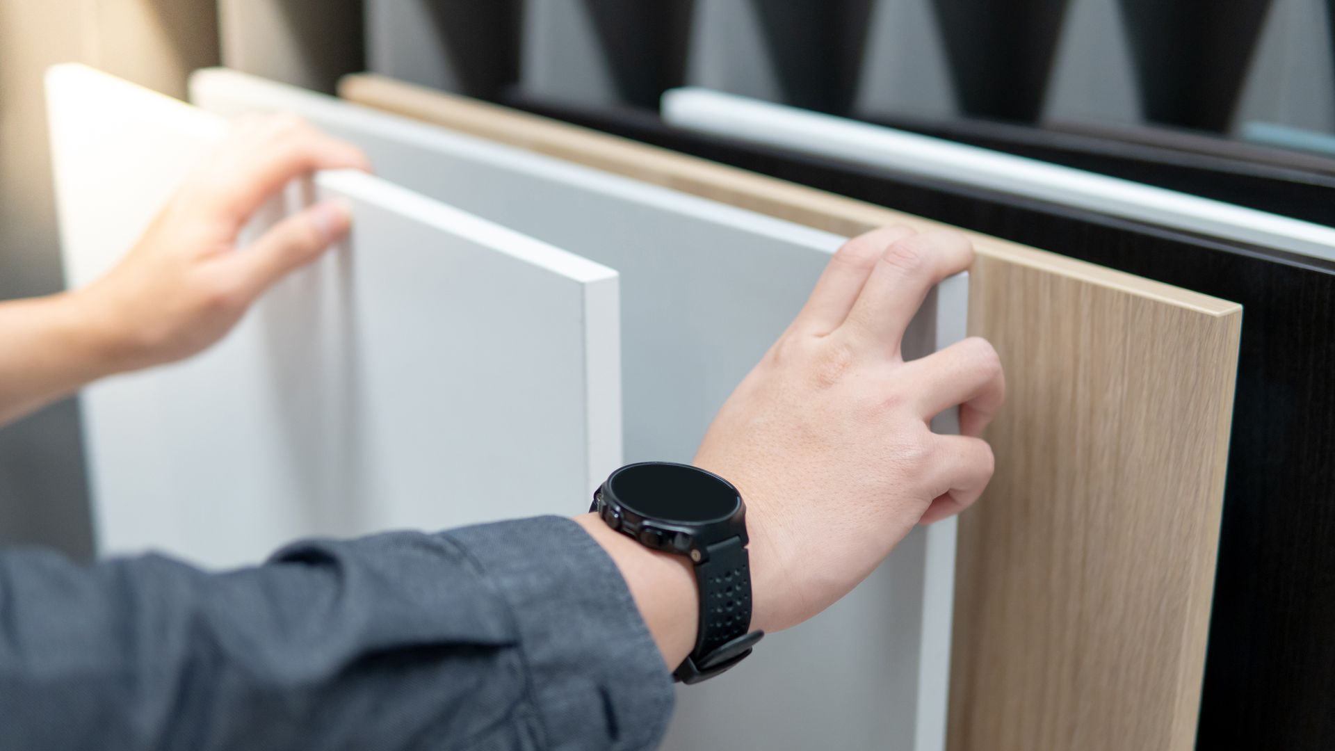 Des mains examinent des échantillons de matériaux pour meubles. Des finitions blanches, grises et imitation bois sont présentées.