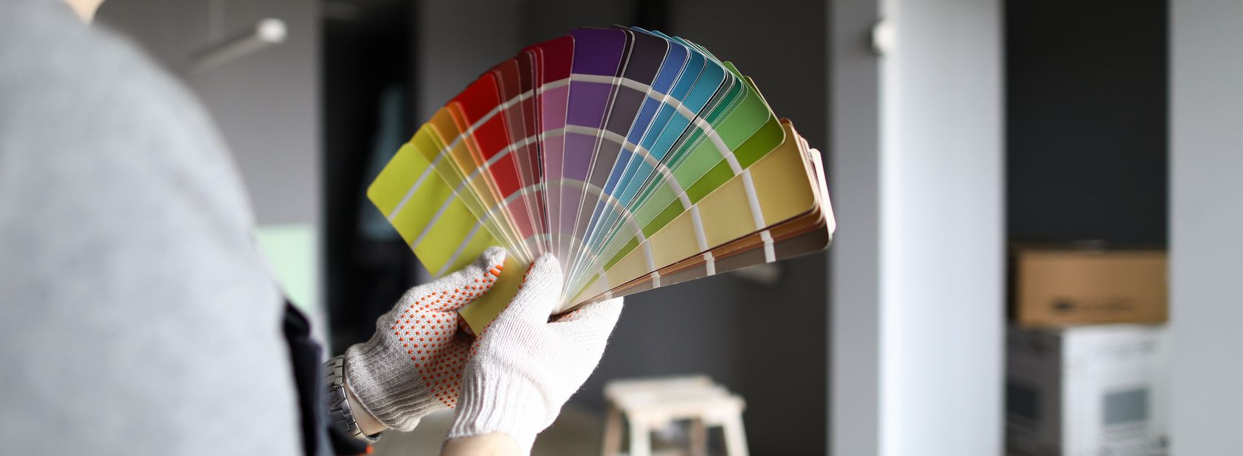 Une personne portant des gants et tenant un éventail d'échantillons de peinture colorés devant un mur.