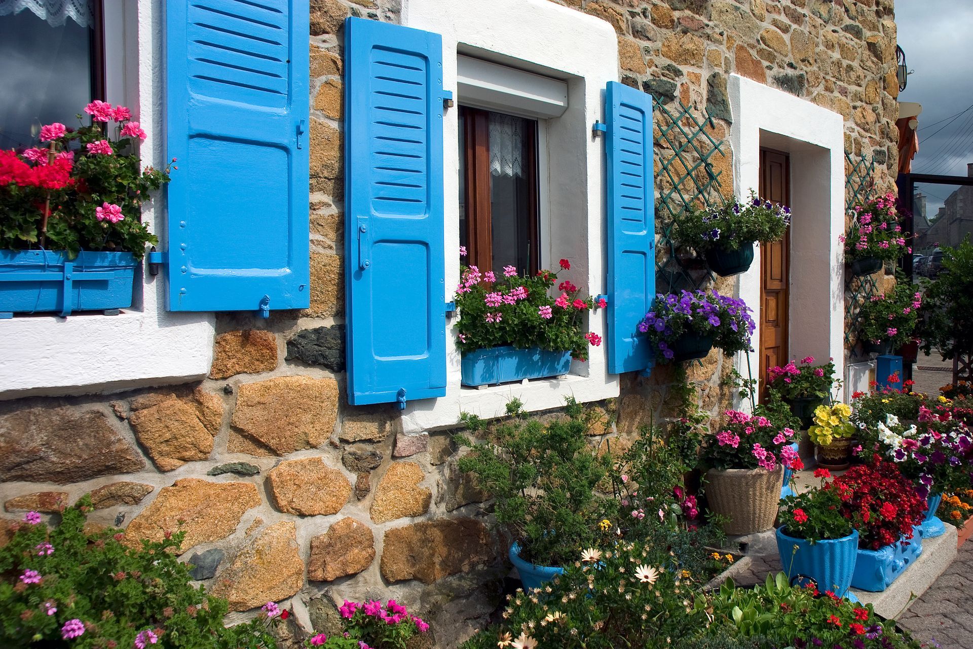 Maison en pierre avec des volets bleus et des jardinières fleuries aux couleurs éclatantes.