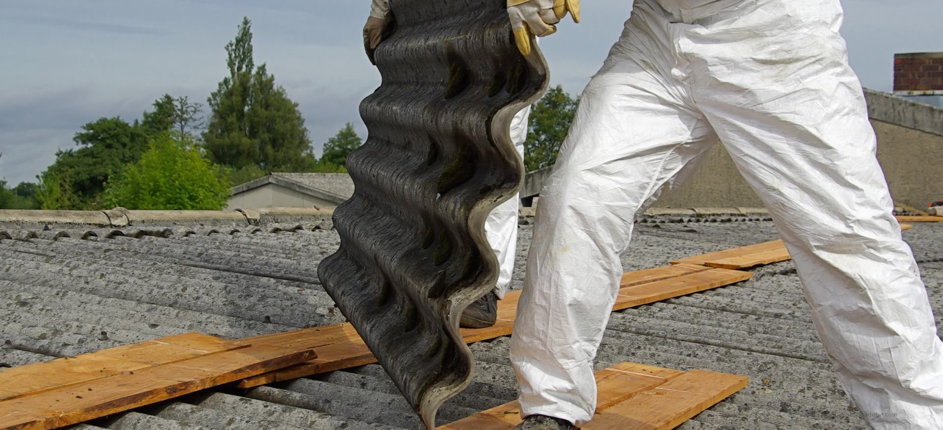 Ein Arbeiter in weißer Hose hält auf einer Kiesbaustelle ein großes schwarzes flexibles Rohr.