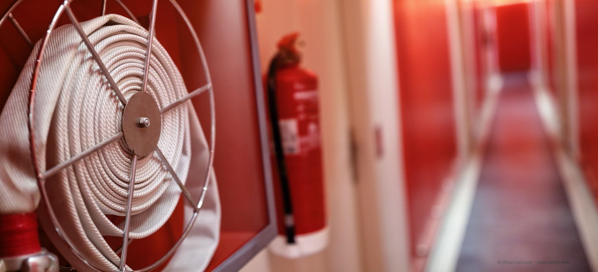 Roter Flur mit einem an der Wand montierten Ventilator und einem Feuerlöscher im Vordergrund