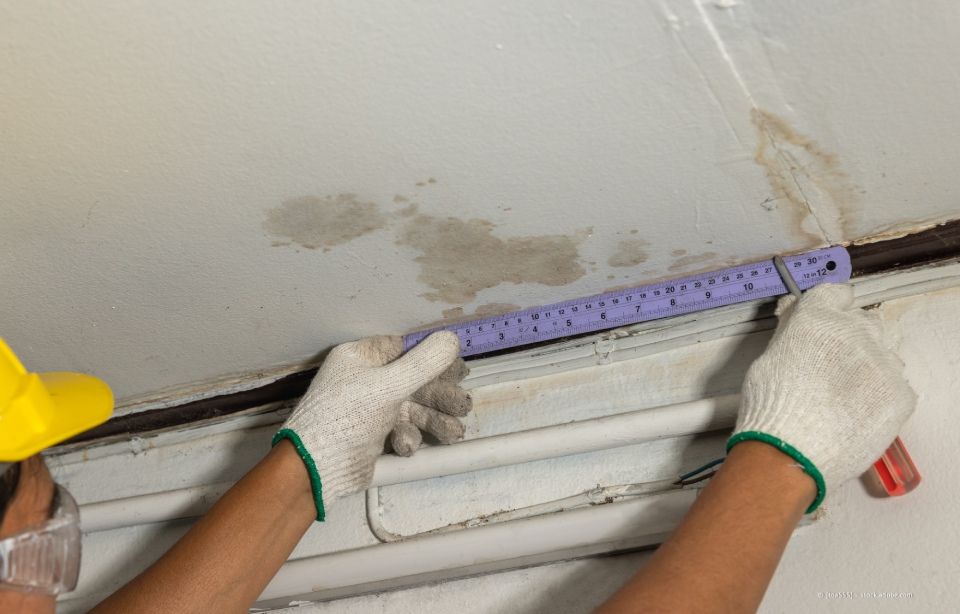Behandschuhte Hände messen mit einem violetten Lineal eine Wand in der Nähe eines Fensterrahmens.