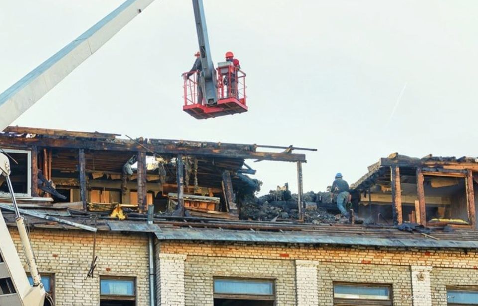 Brandschäden auf einem Dach, während Feuerwehrleute von einem Kran aus über einem abgebrannten Gebäude arbeiten.