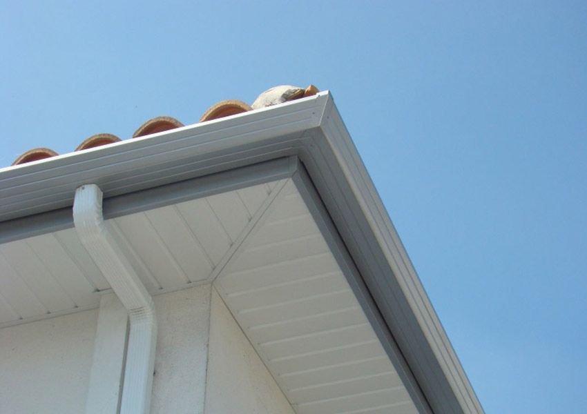 Gros plan sur la toiture et la gouttière d'une maison blanche se détachant sur un ciel bleu clair.