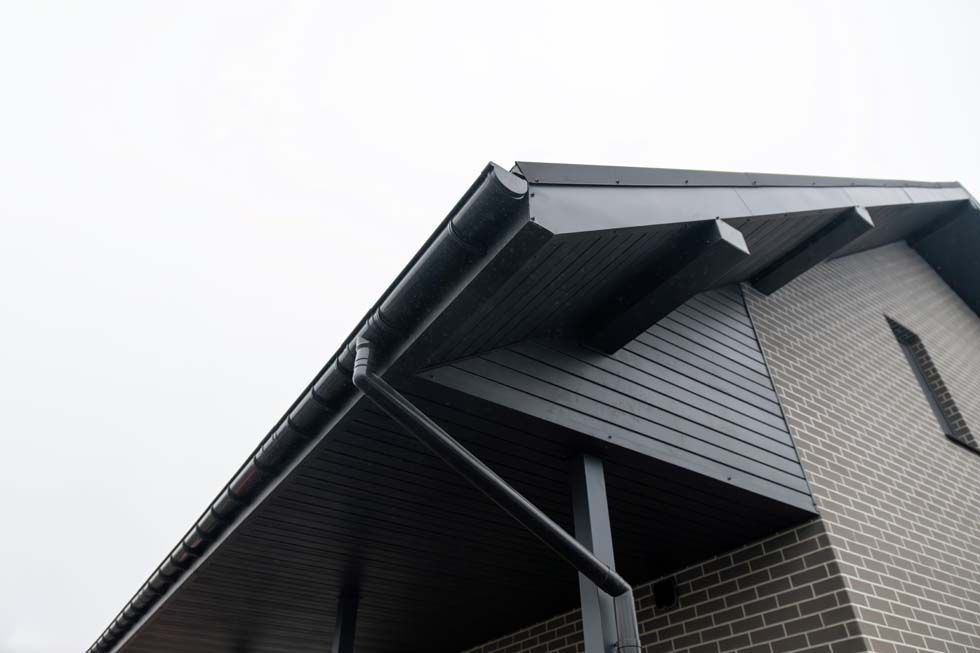 Gros plan sur le toit d'une maison avec un bardage gris foncé et des avant-toits apparents sur un ciel nuageux