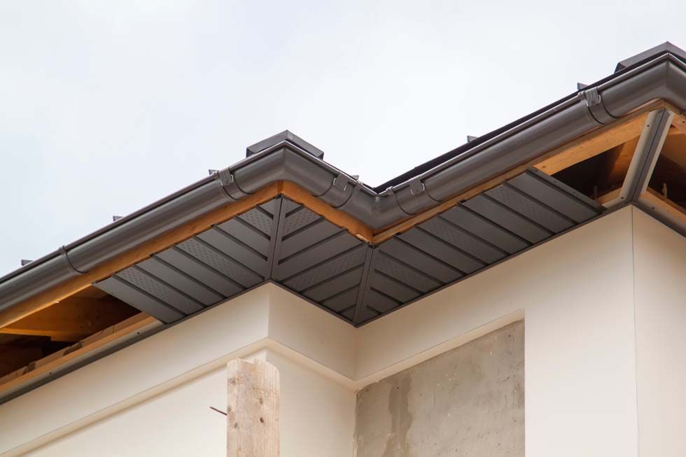 Gros plan sur le toit d'une maison aux bardeaux gris et aux avant-toits en bois apparents, se détachant sur un ciel pâle.