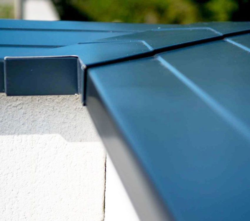 Bordure de toit en métal bleu au-dessus d'un mur extérieur blanc avec de la verdure floue en arrière-plan