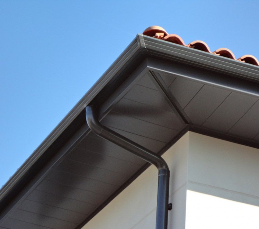 Gros plan sur l'avant-toit d'une maison avec des gouttières grises se détachant sur un ciel bleu.