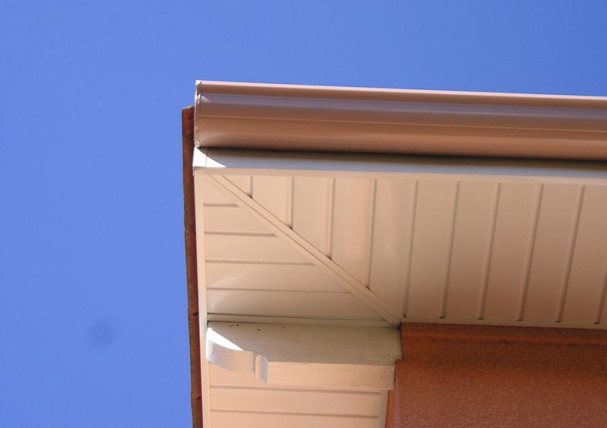 Coin de toit de maison avec soffite beige et gouttière brune sur fond de ciel bleu
