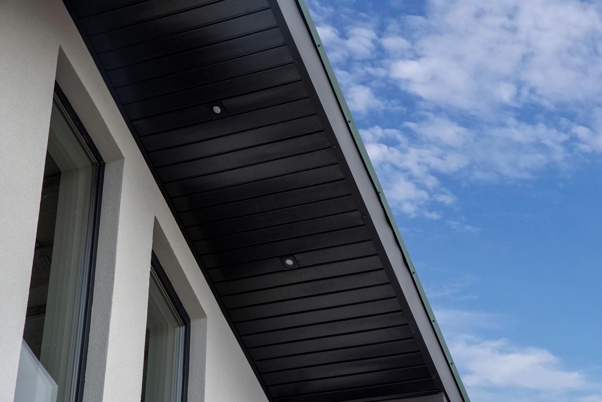 Toiture d'un bâtiment moderne se détachant sur un ciel bleu partiellement nuageux
