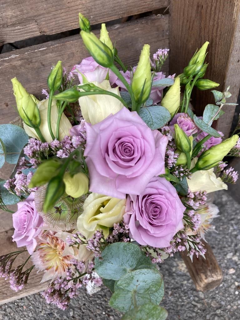 Ein Strauß lila Rosen und weißer Blumen steht auf einem Holztisch.