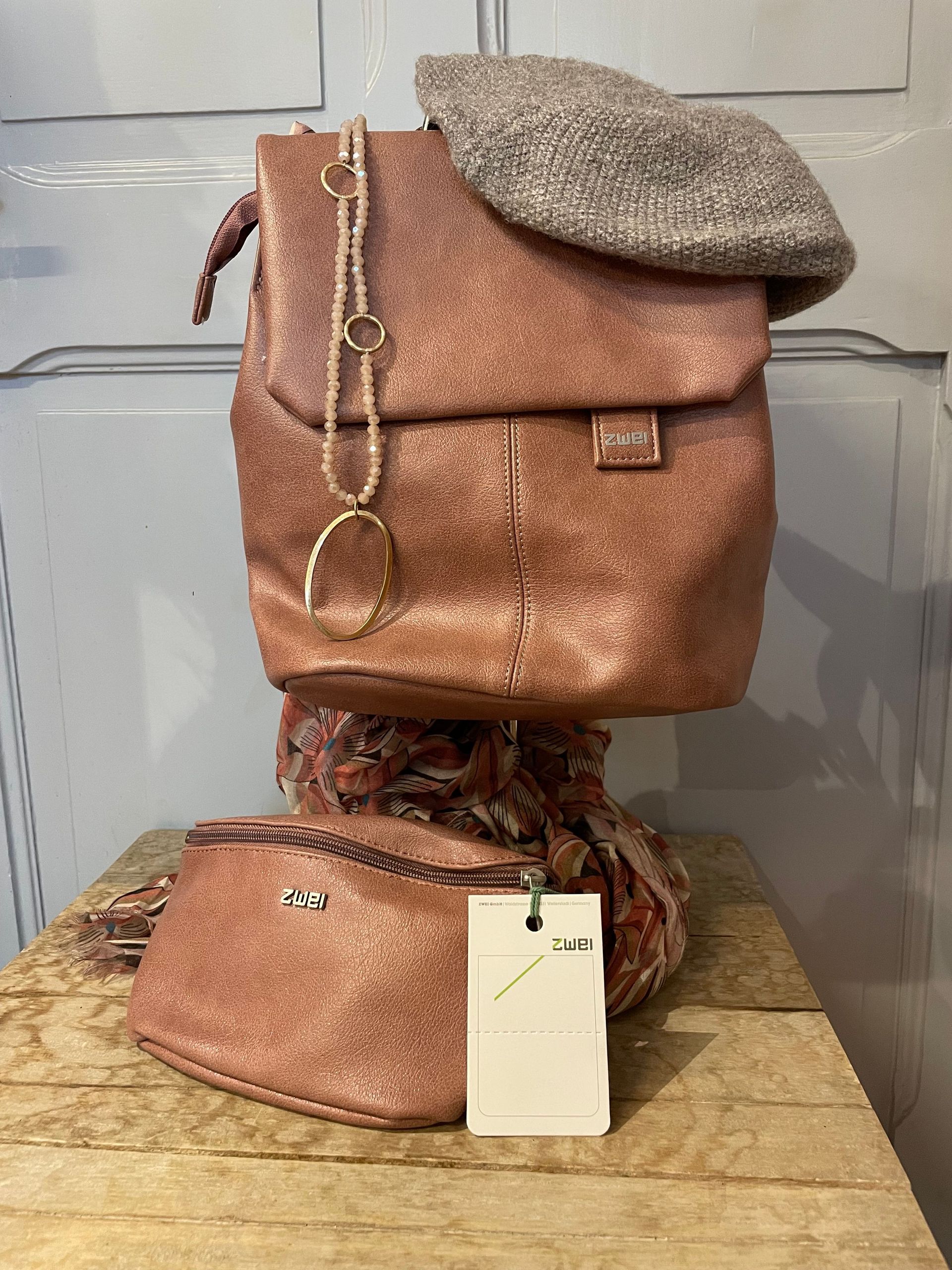 Eine rosa Handtasche und ein Hut liegen auf einem Holztisch.