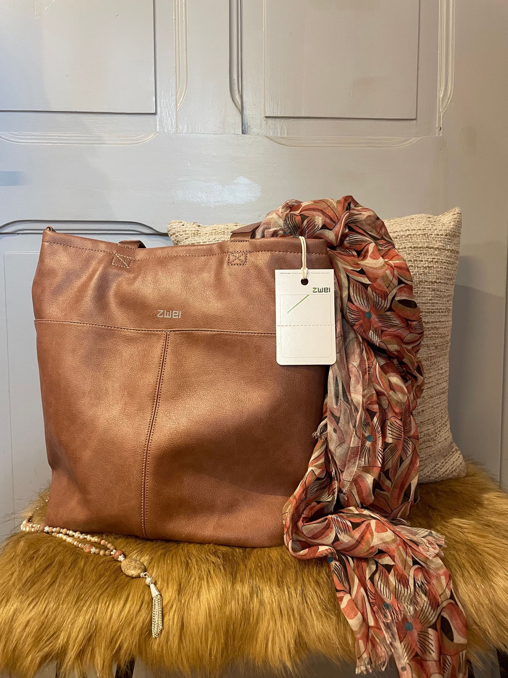 Eine braune Einkaufstasche und ein Schal liegen auf einem pelzigen Stuhl.