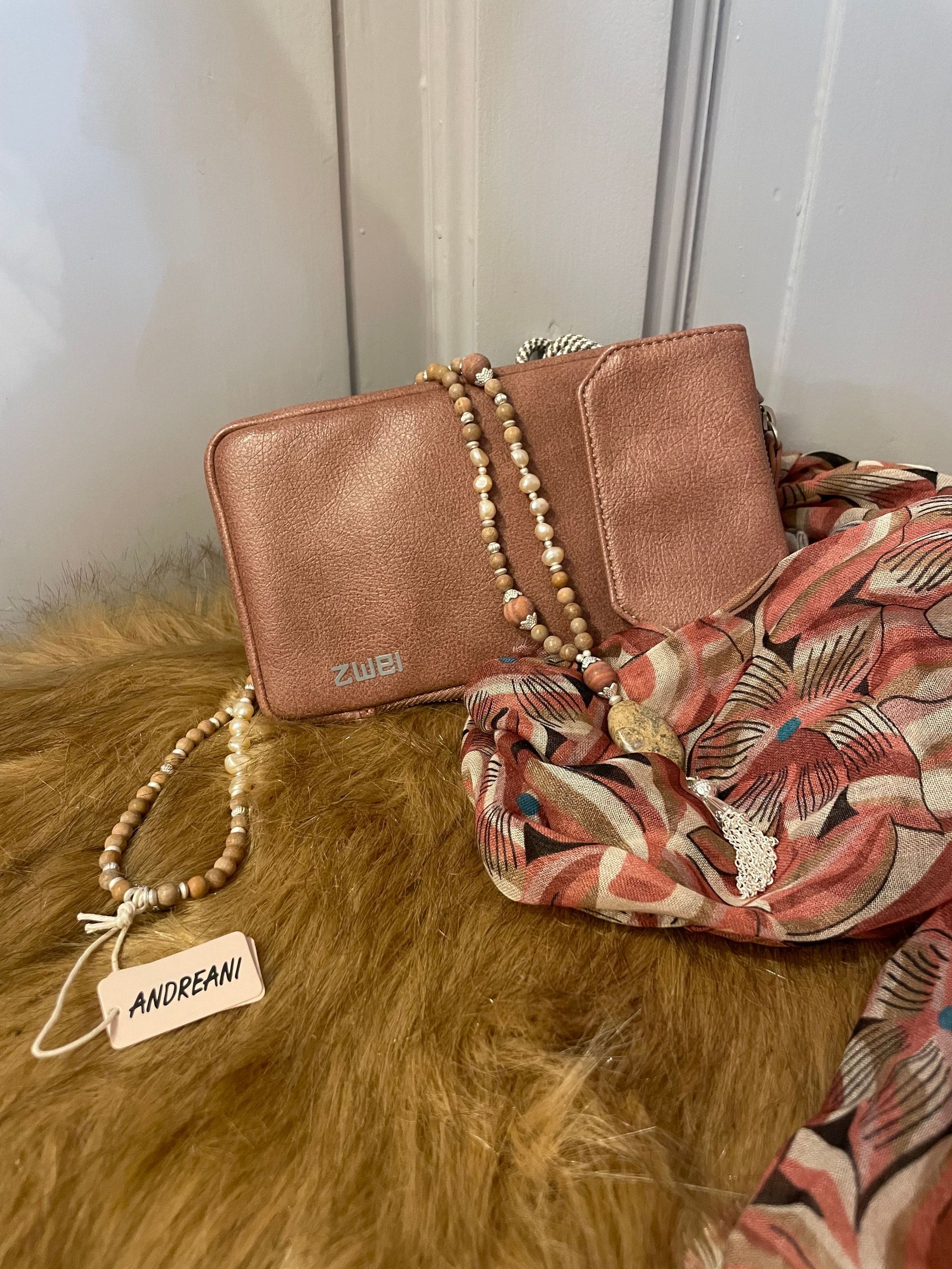 Eine rosa Handtasche liegt neben einem Schal auf einem Pelzteppich.