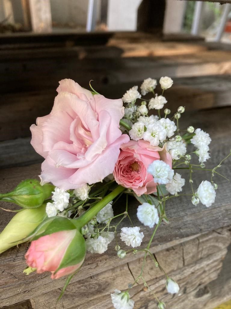 Eine Nahaufnahme einer rosa Rose und Schleierkraut auf einem Holztisch.