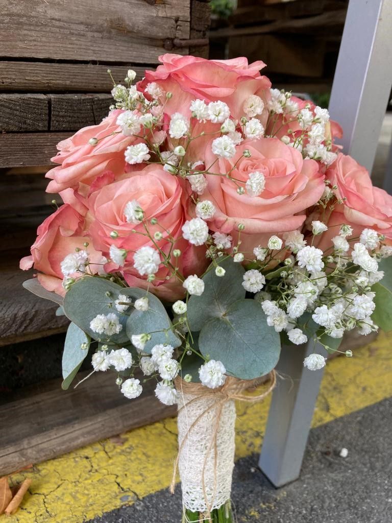Auf einem Tisch steht ein Strauß rosa Rosen und Schleierkraut.