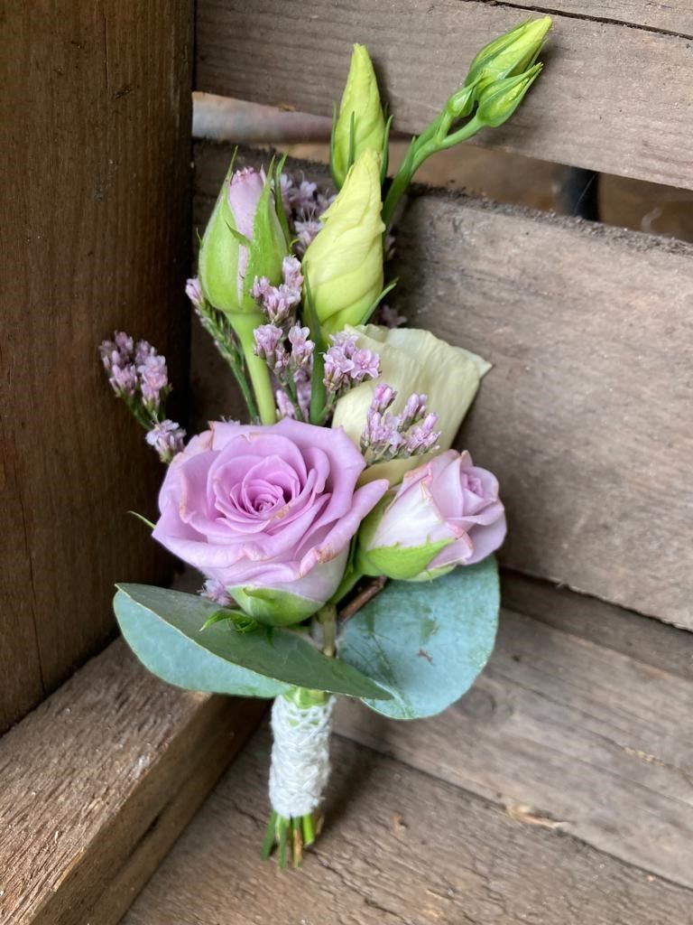 Ein kleiner Strauß lila Rosen und Grünpflanzen steht auf einem Holztisch.