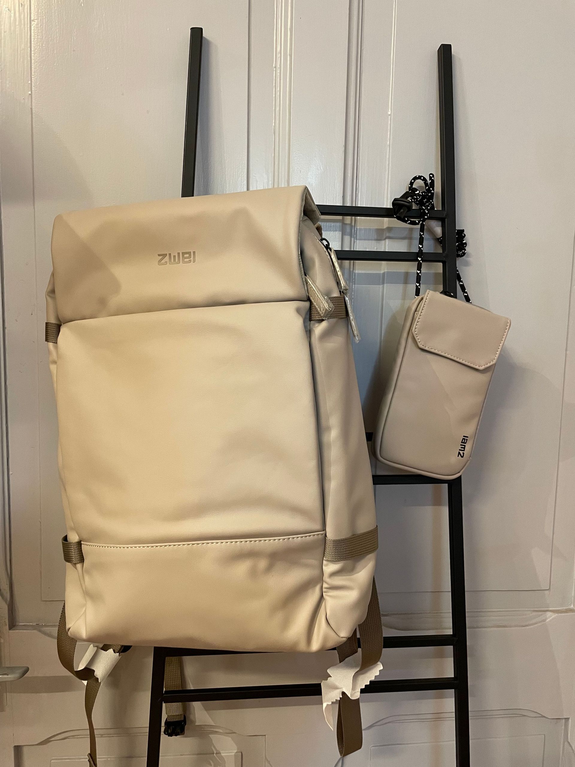 Ein weißer Rucksack hängt neben einer Handtasche an einer Leiter.