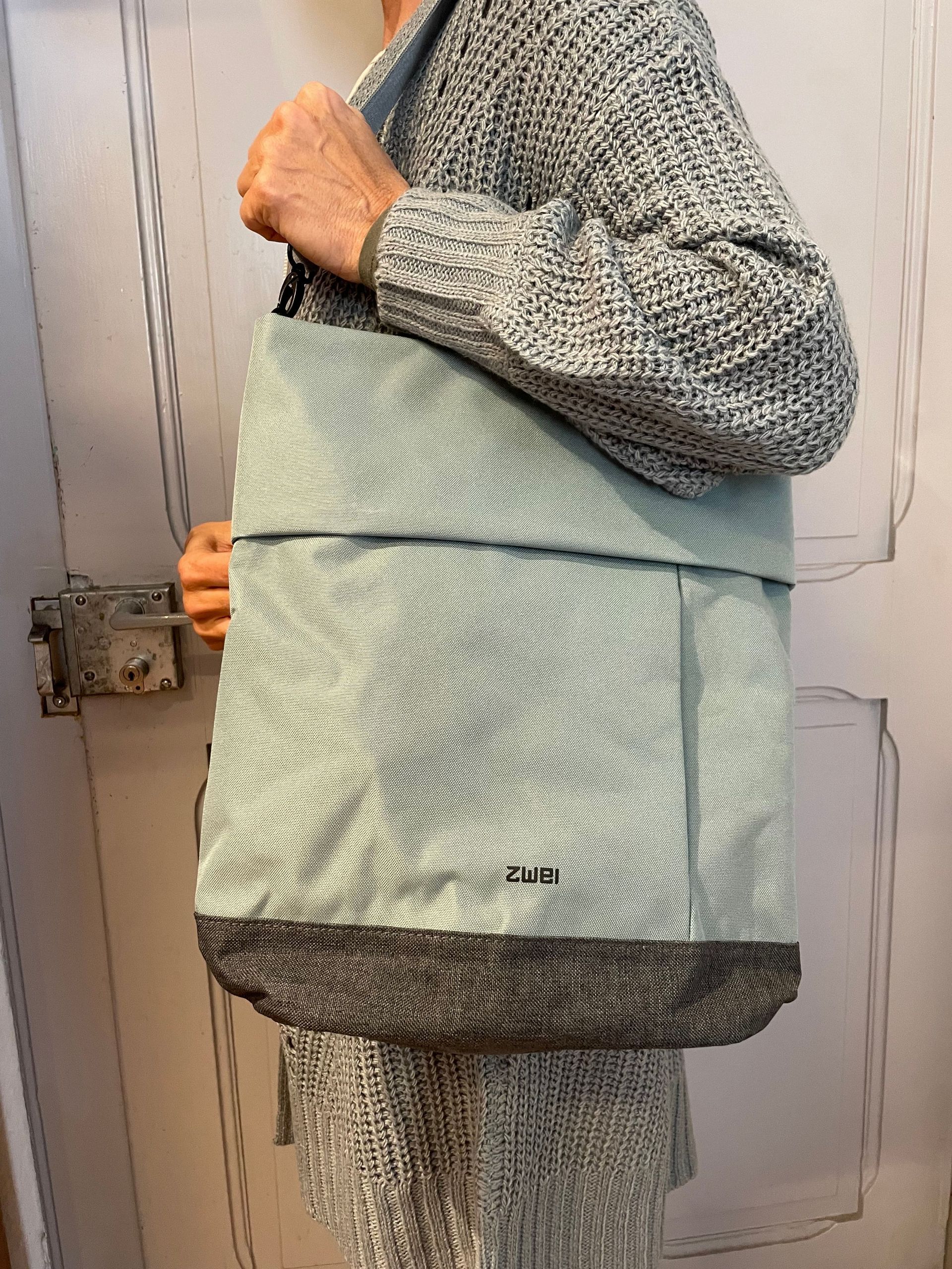 Eine Frau im Pullover hält eine grüne Einkaufstasche.